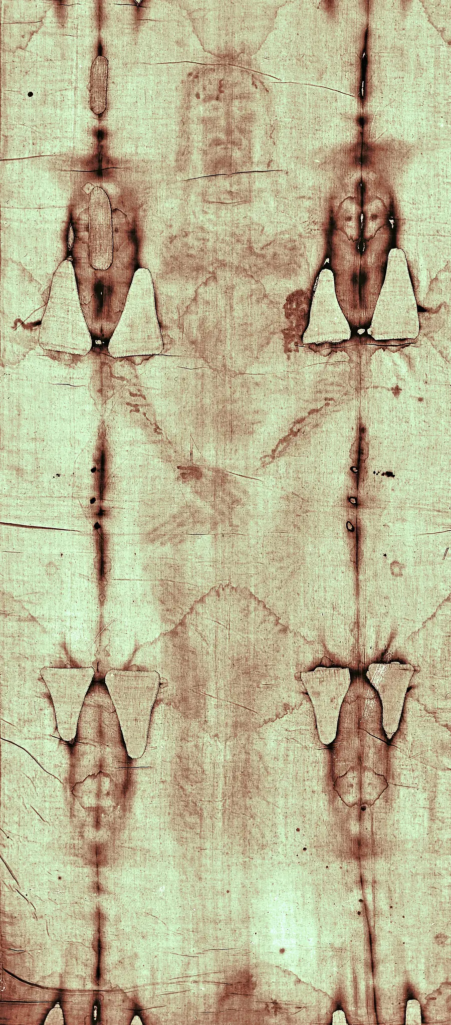 Die Vorderseite des Mannes auf dem Grabtuch, blass bräunlich auf hellem Leinen, beiderseits begrenzt von dunklen Brandlinien und hellen Flicken des Brandes von 1532.